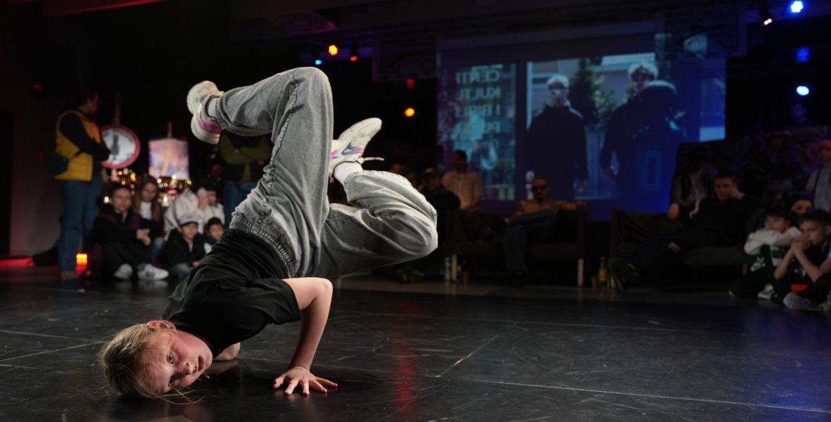 Dziewczyna tańczy będąc głową w dół, za nią widzowie