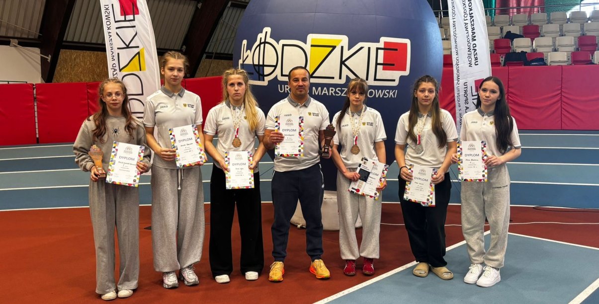 Sześć zapaśniczek w hali sportowej, pośrodku trener