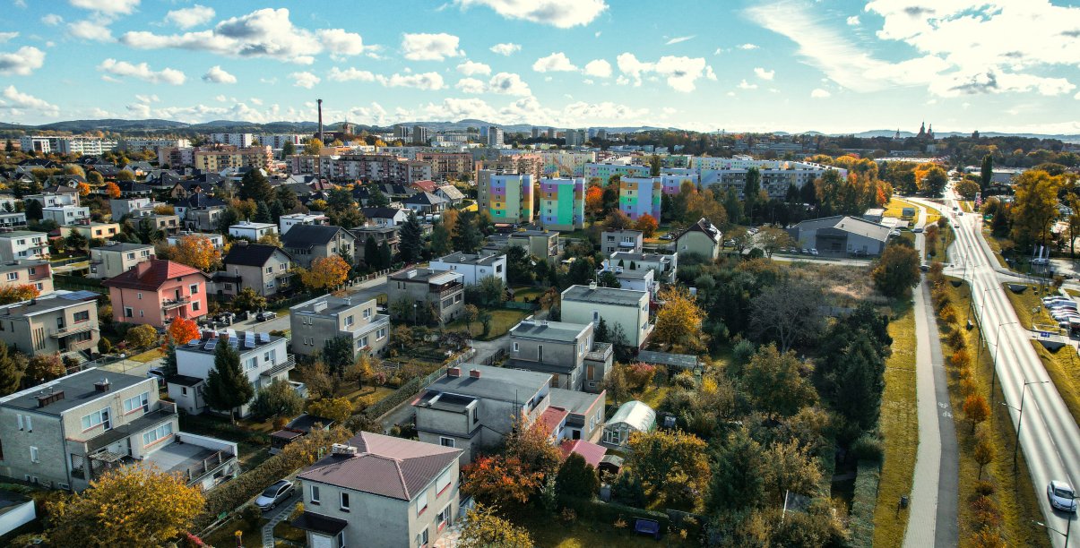 Miasto z góry, na pierwszym planie domki jednorodzinne, za nimi osiedla, dalej góry 