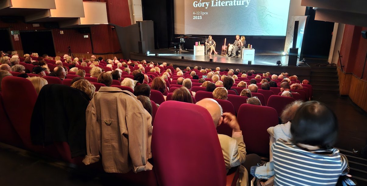 Wypełniona widownia kinoteatru, na scenie dyskusja trzech osób, za nimi na dużym ekranie napis Góry Literatury