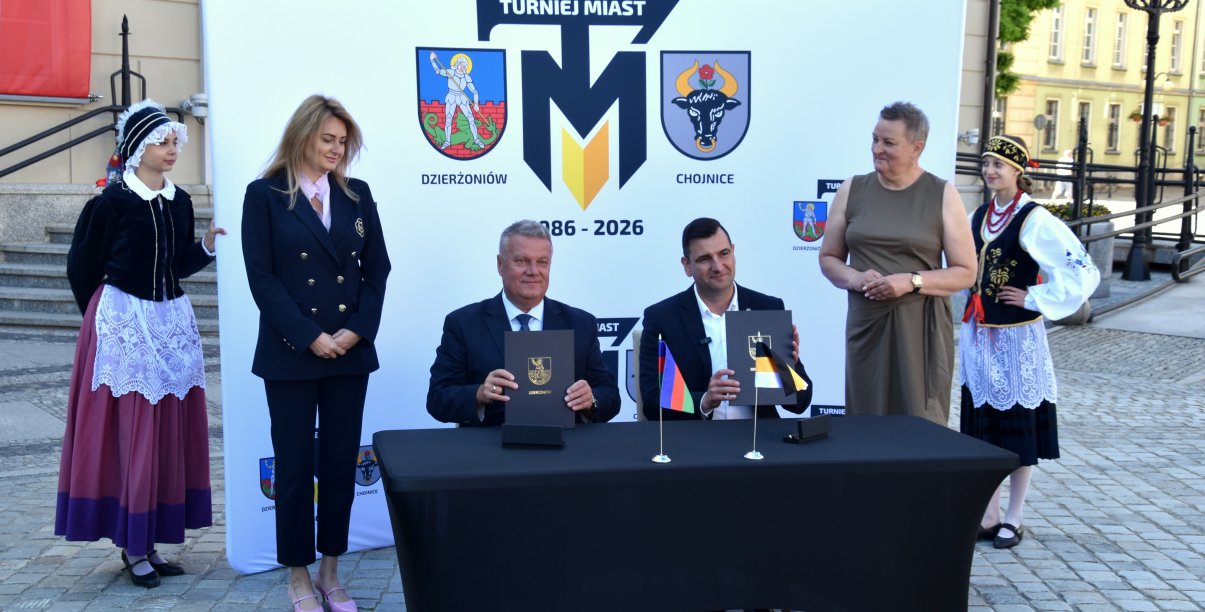 Burmistrz Dzierżoniowa i Chojnic siedzą przy stole, trzymają pospisane umowy