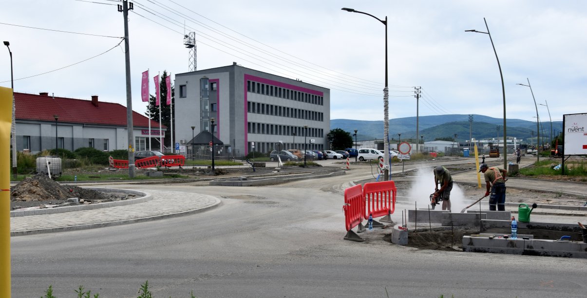 Rondo i droga w budowie, przy rondzie pracownicy w tle niewielki biurowiec