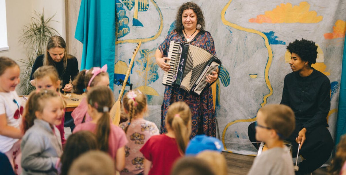 Kobieta grająca na harmonii, przed nią grupa dzieci