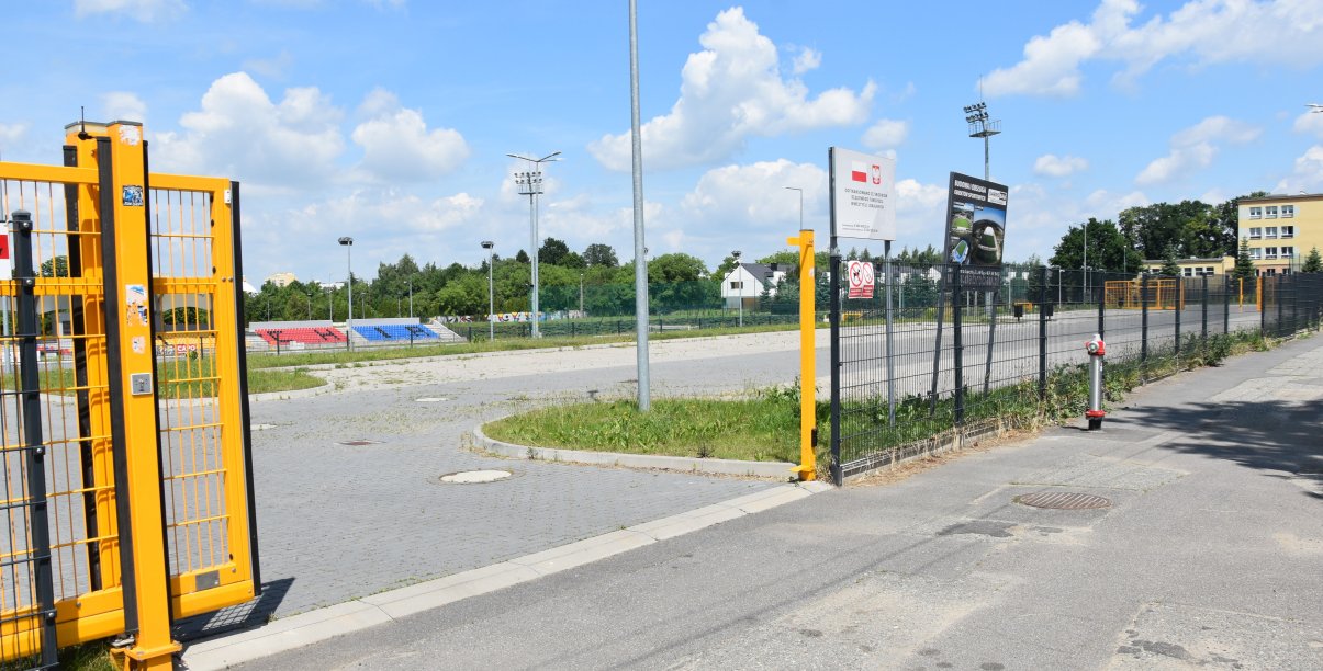 Żółta, otwarta brama przed dużym parkingiem z kostki betonowej