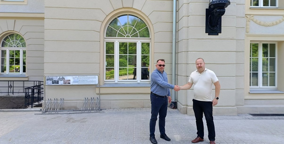 Prezes uzdrowiska i zastępca burmistrza ściskają sobie dłonie, w tle budynek