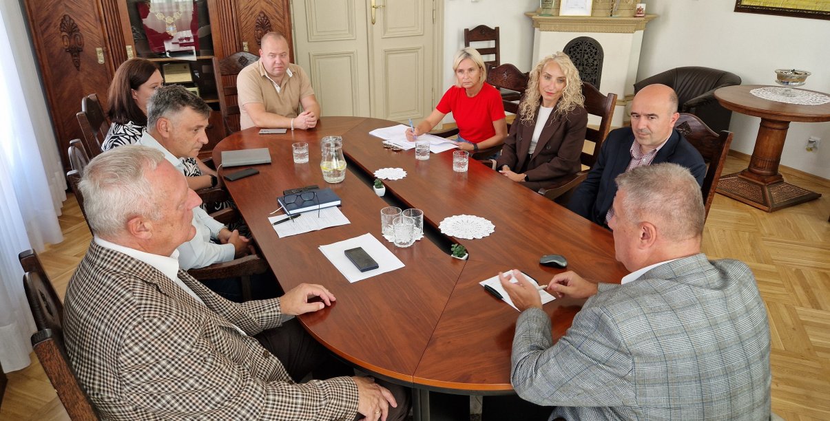 Ośmioro uczestników spotkania siedzących przy owalnym stole w gabinecie burmistrza