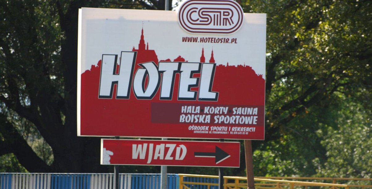 Duży baner przy drodze dojazdowej do ośrodka sportu z napisem hotel