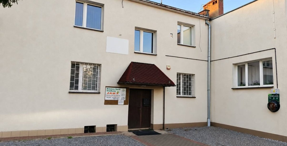 Dwupiętrowy budynek, przy wejściu zamontowany zewnętrzny defibrylator