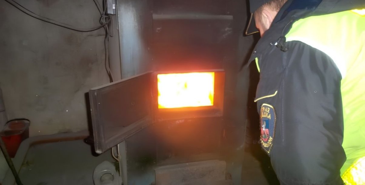 Strażnik miejski w żółtej kamizelce zaglądający do wnętrza pieca