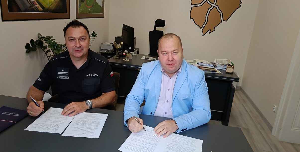 Zastępca burmistrza i komendant aresztu przy biurku podpisują porozumienie