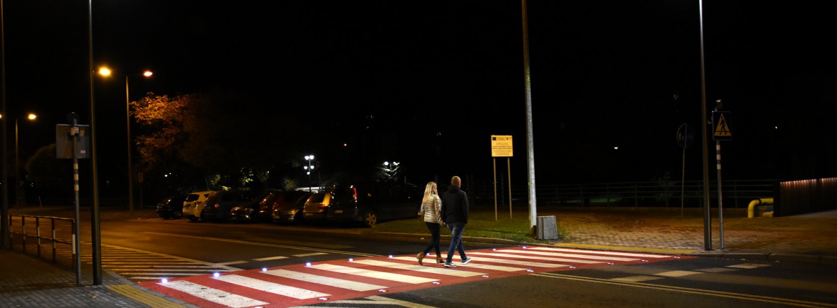 Dobrze oświetlone przejscie dla pieszych, przez które przechodzi para mieszkańców