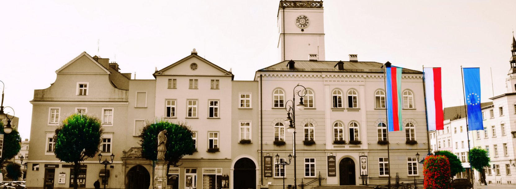 Czano-biały budynek ratusza i kolrowe flagi UE, Polski i Dzierżoniowa
