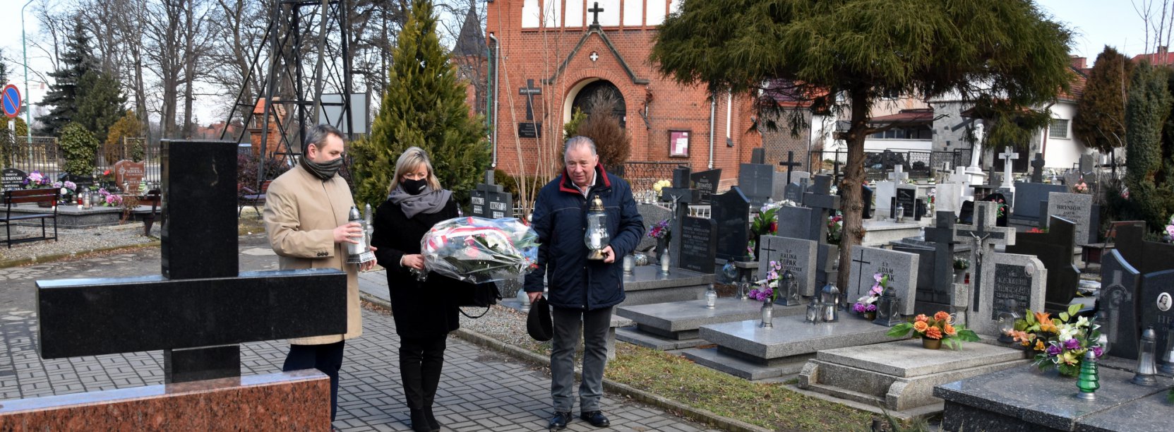 Trzy osoby składają wiążankę kwiatów przy pomniku na dzierżóniowskim cmentarzu 