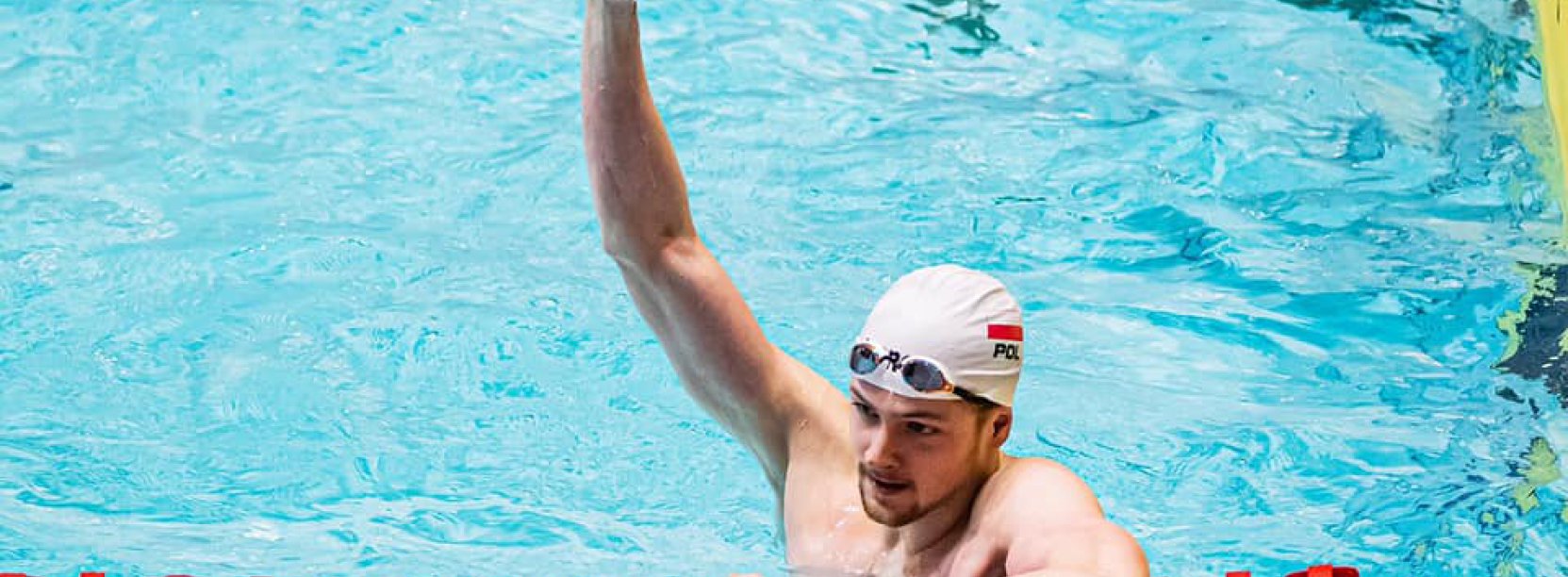 Paweł Juraszek w basenie z ręką podniesioną w geście zwycięstwa