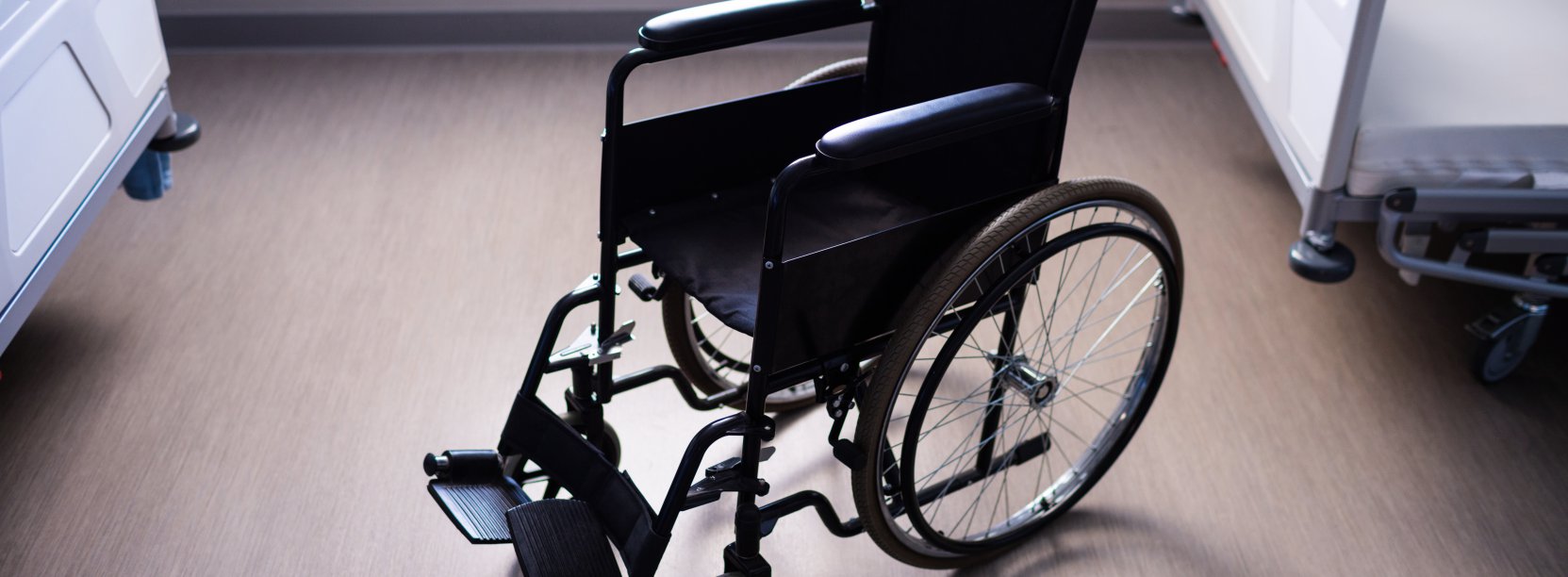 Na zdjęciu puste łóżka rehabilitacyjne i wózek inwalidzki 
