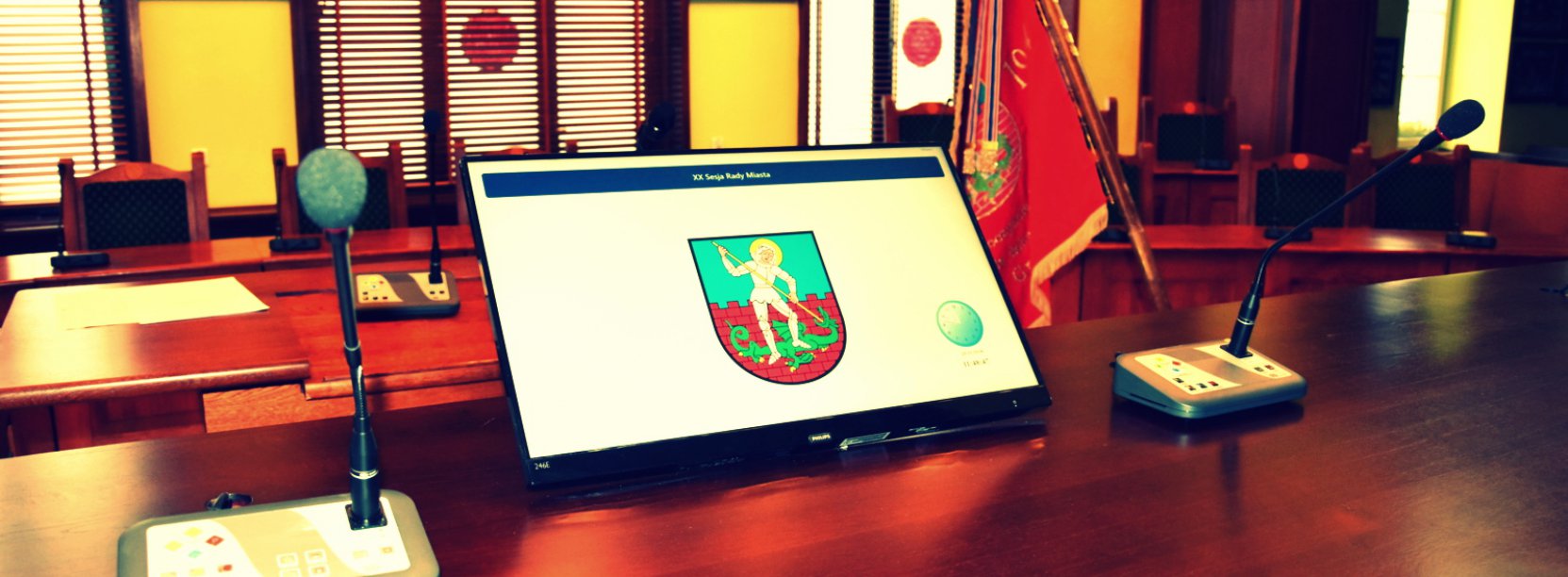 Stół prezydialny, na nim monitor z herbem Dzierżoniowa