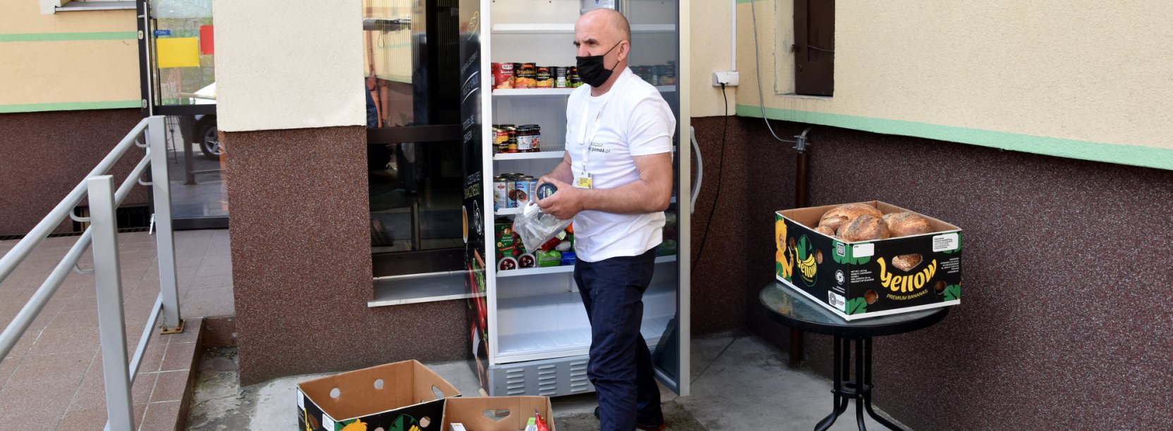 Mężczyzna wkładający jedzenie do lodówku przy wejściu do budynku OPS-u