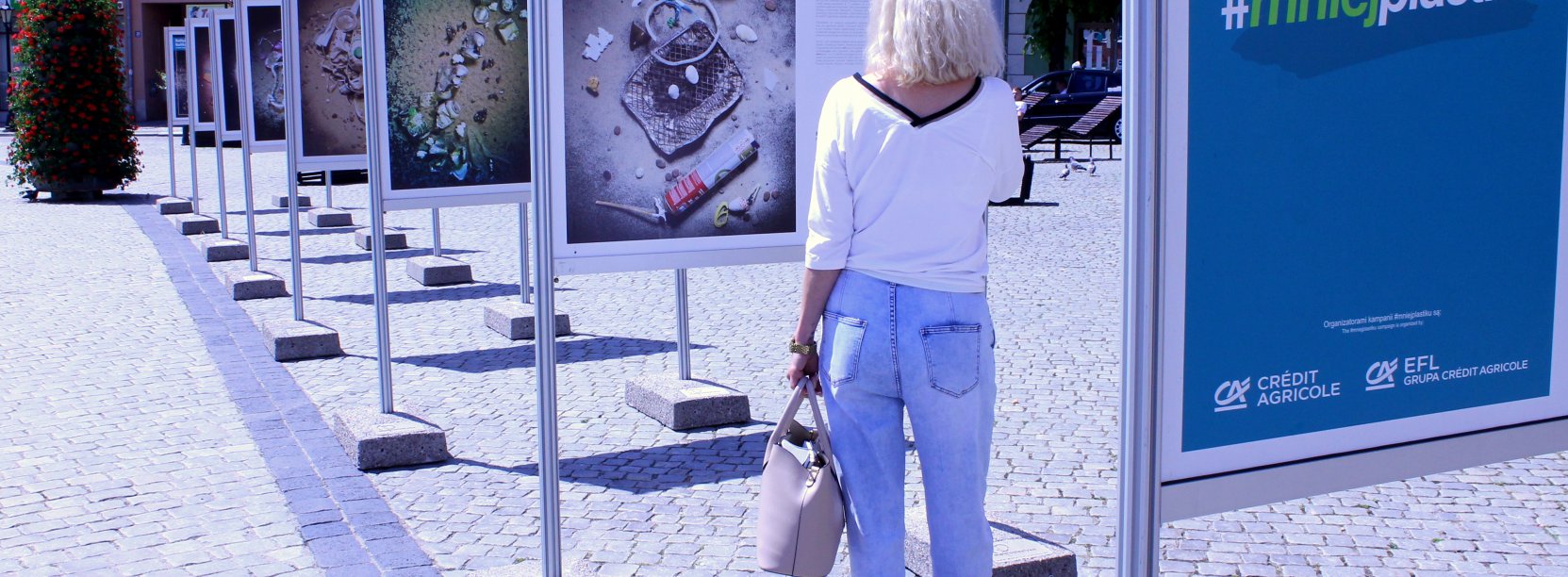 Kobieta w białej bluzce stojąca tyłem do obiektywu oglądająca wystawę