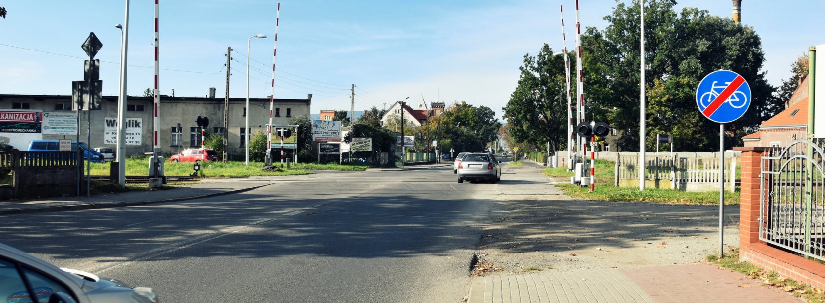 Przejad kolejowy, podniesione szlabany, w drugim planie droga