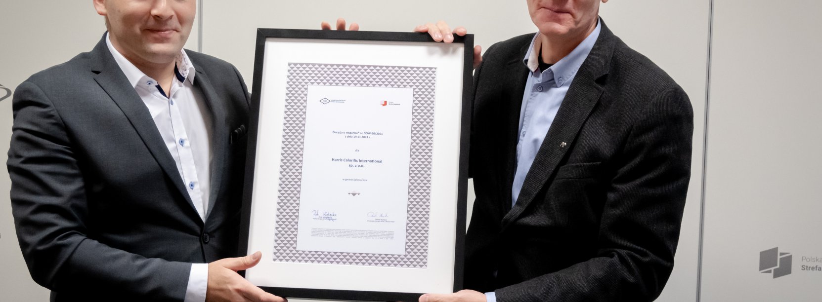 Dwóch pamów w garniturach trzymających oprawiony dyplom 