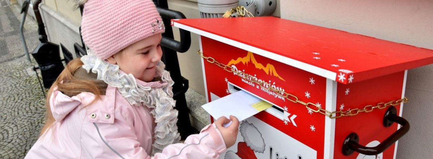 Uśmiechnięta dziewczynka wrzucająca list do czerwonej skrzynki 