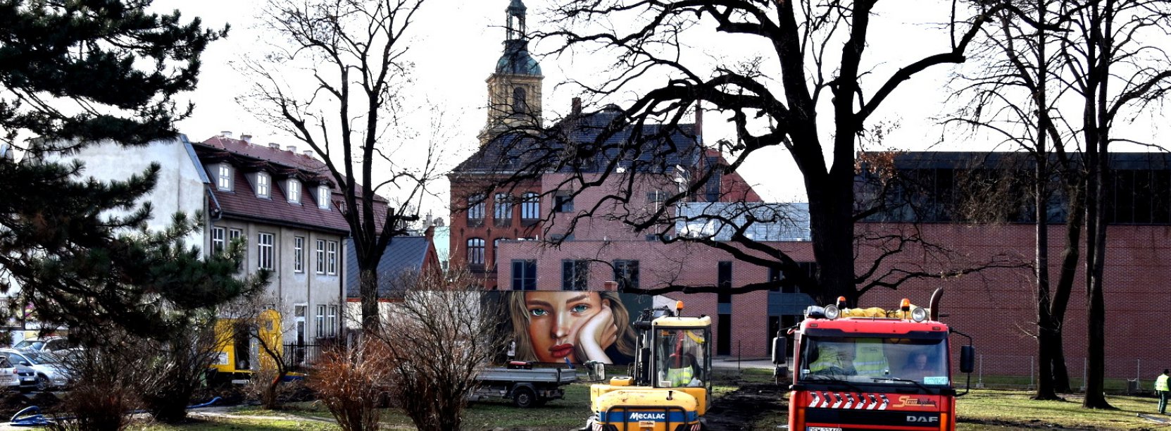 Park późną jesienią, pracująca koparka i stojący obok smochód ciężarowy