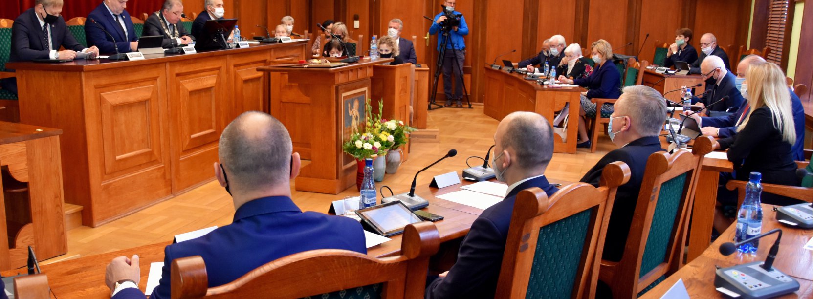 Duża sala, radni siedzący tyłem do obiektywu, w druim planie widok prezydium rady