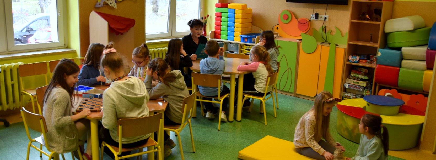 Świetlica szkolna, dzieci siedzące przy stołach i bawiące się wspólnie
