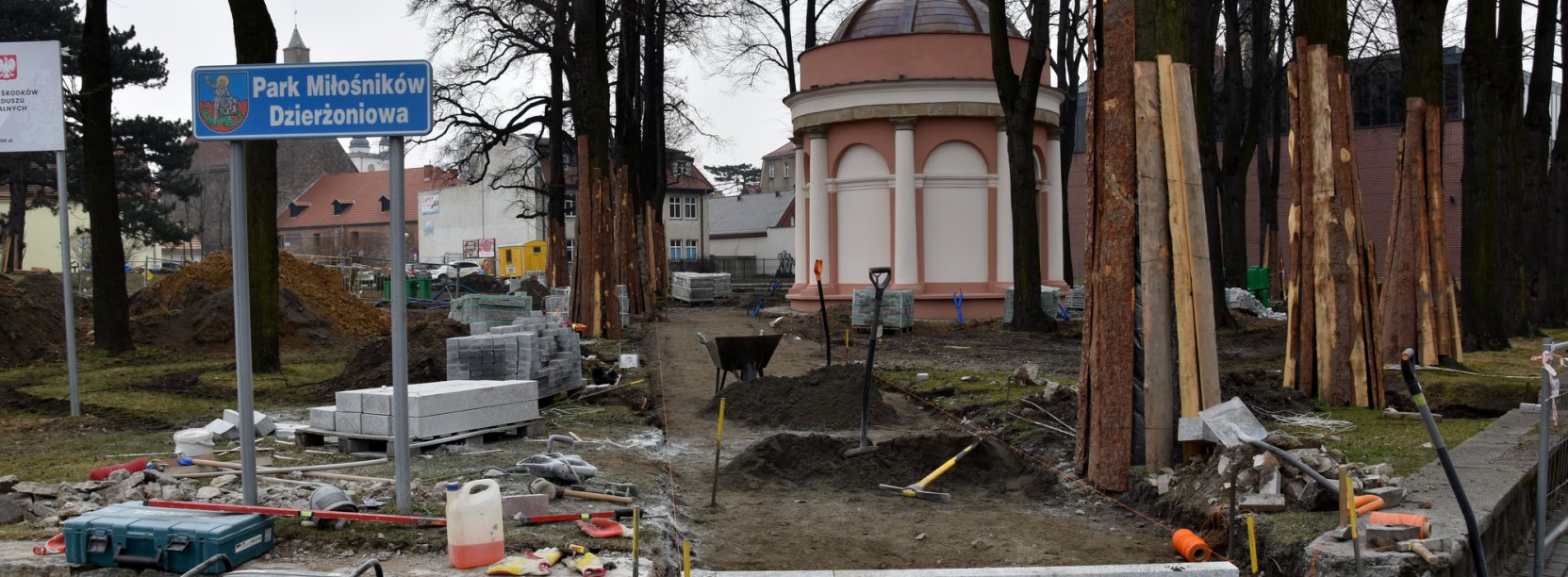 Park, w trackie remontu, drzewa zabezpieczone deskami i schody na pierwszym planie 