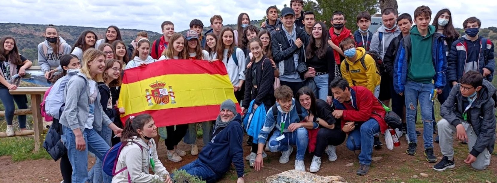 Grupowe zdjęcie kilkunastu osób w górach i flaga Hiszpanii
