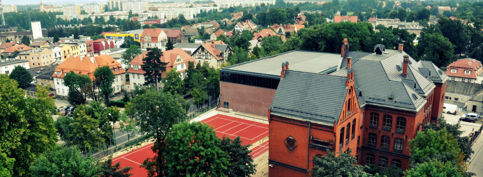 Fragment miasta z góry, na pierwszym planie duży budynek z cegły i boisko 