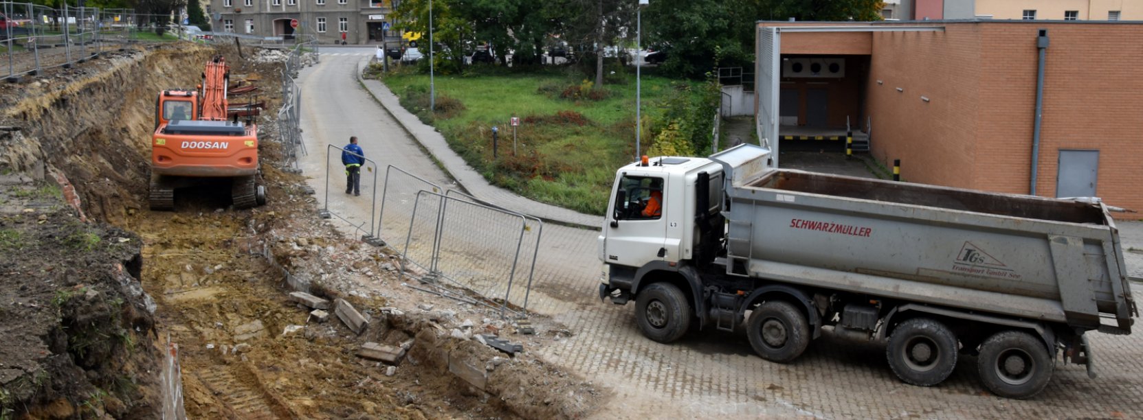 Koparka i auto ciężąrowe stojące przy remontowanej drodze