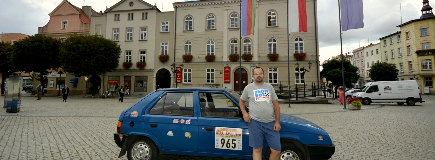 Mężczyzna stojący przy samochodzie, w drugim planie ratusz