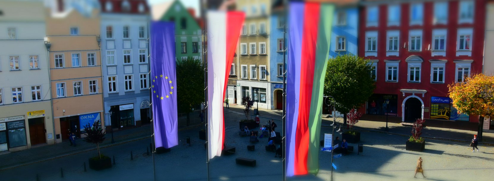 Maszty z flagami Polski, UE i Dzierżoniowa, z tyłu zabytkowe kamienice