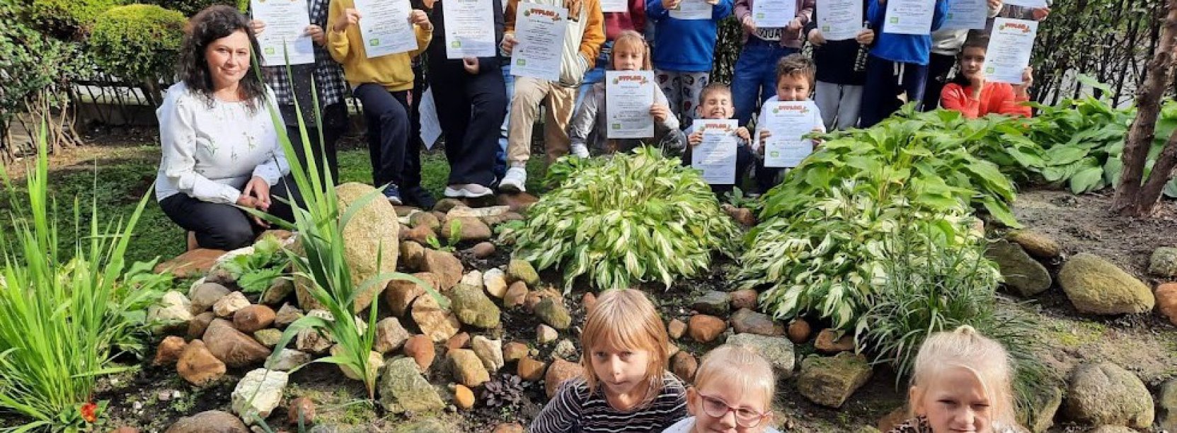 Grupowe zdjęcie dzieci trzymających dyplony, dookoła zieleń 