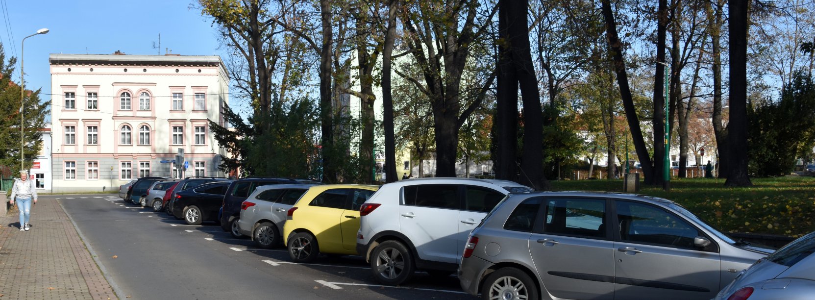 Ulica w mieście, po prawej zaparkowane auta, w drugim planie duża kamienica