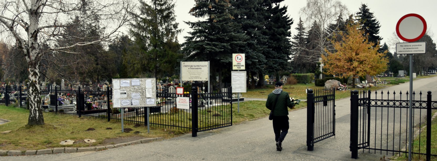 Mężczyzna z wiązanką kwiatów wchodzący na teren cmentarza 