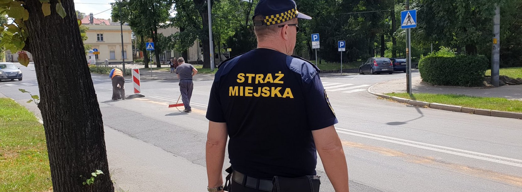 Strażnik stojący tyłem w służbowym stroju, w drugim planie droga i zieleń