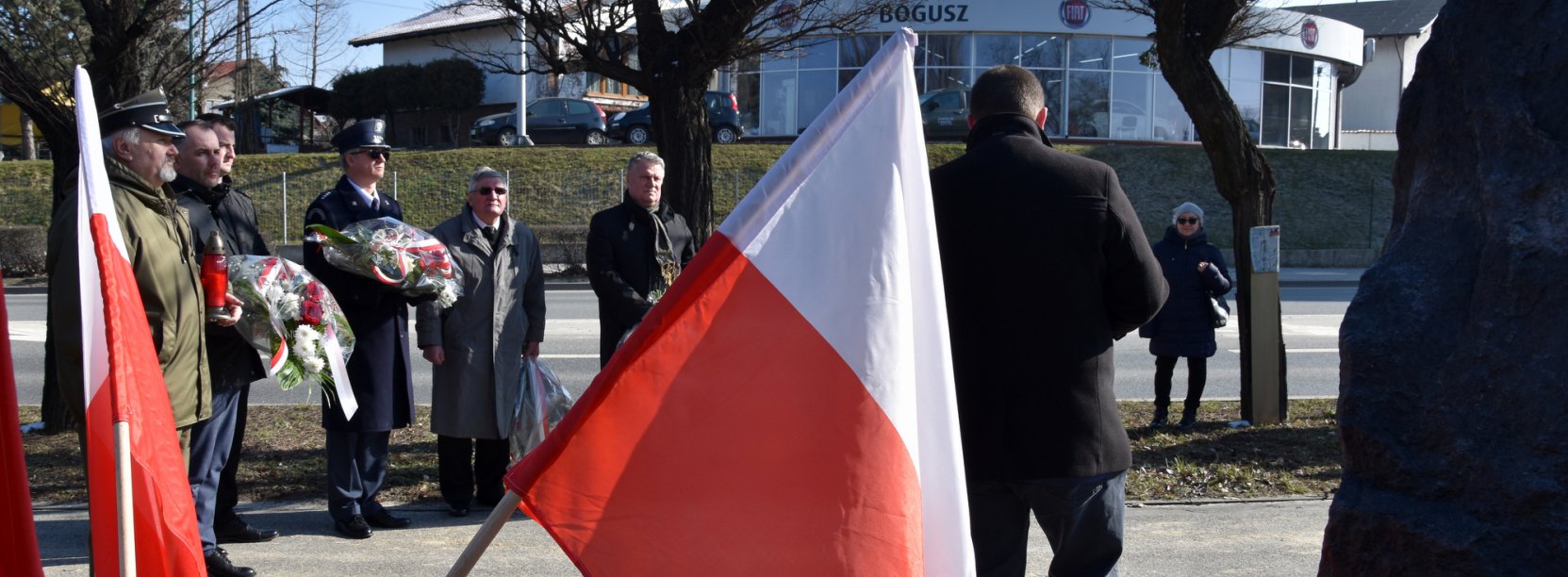 Falag Polski na pierwszym planie, w drugim pplanie grupa osób stojąca przy ulicy