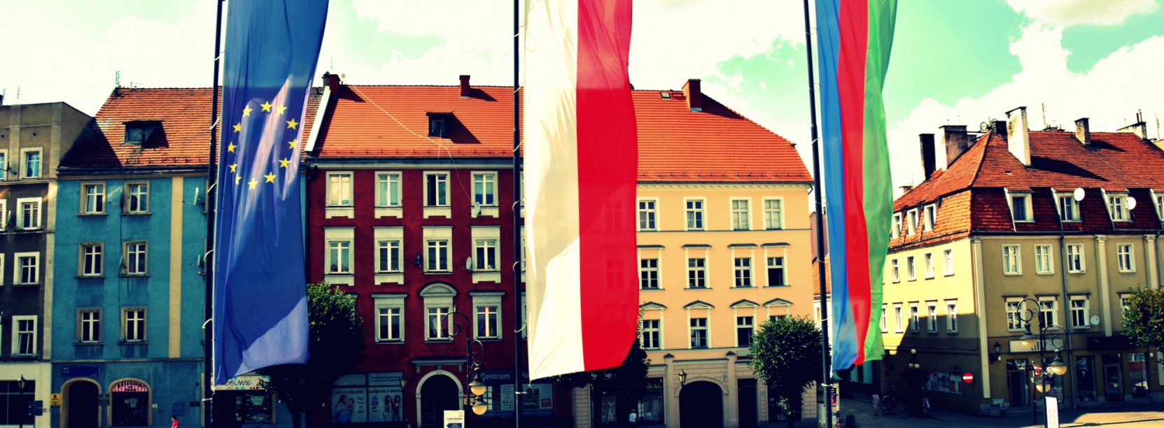 Flagi Unii Europejskiej, Polski i Dzierżoniowa na masztach, w tle kamienice