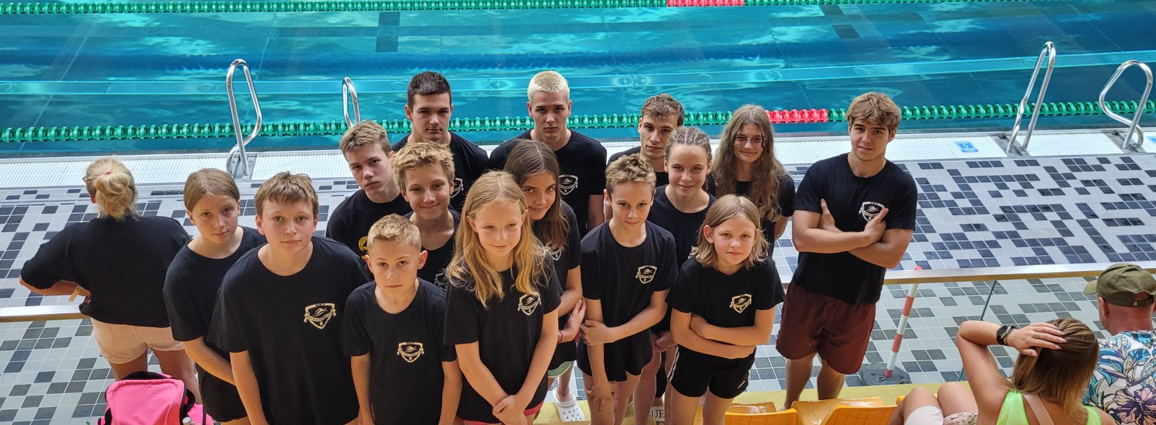 Grupowe zdjęcie pływaków w czarnych koszulkach przy basenie