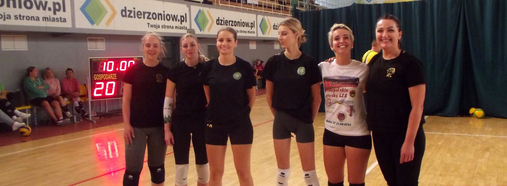 Sześć usmiechniętych siatkarek na wspólnym zdjęciu w halisportowej, w tle reklama strony www.dzierzoniow.pl