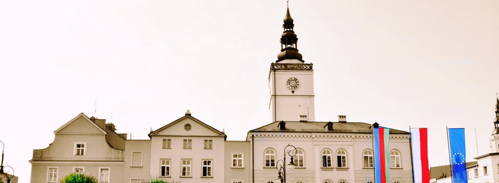 Budynek ratusza, przed nim trzy masty i flagi Polski, UE i Dzierżoniowa