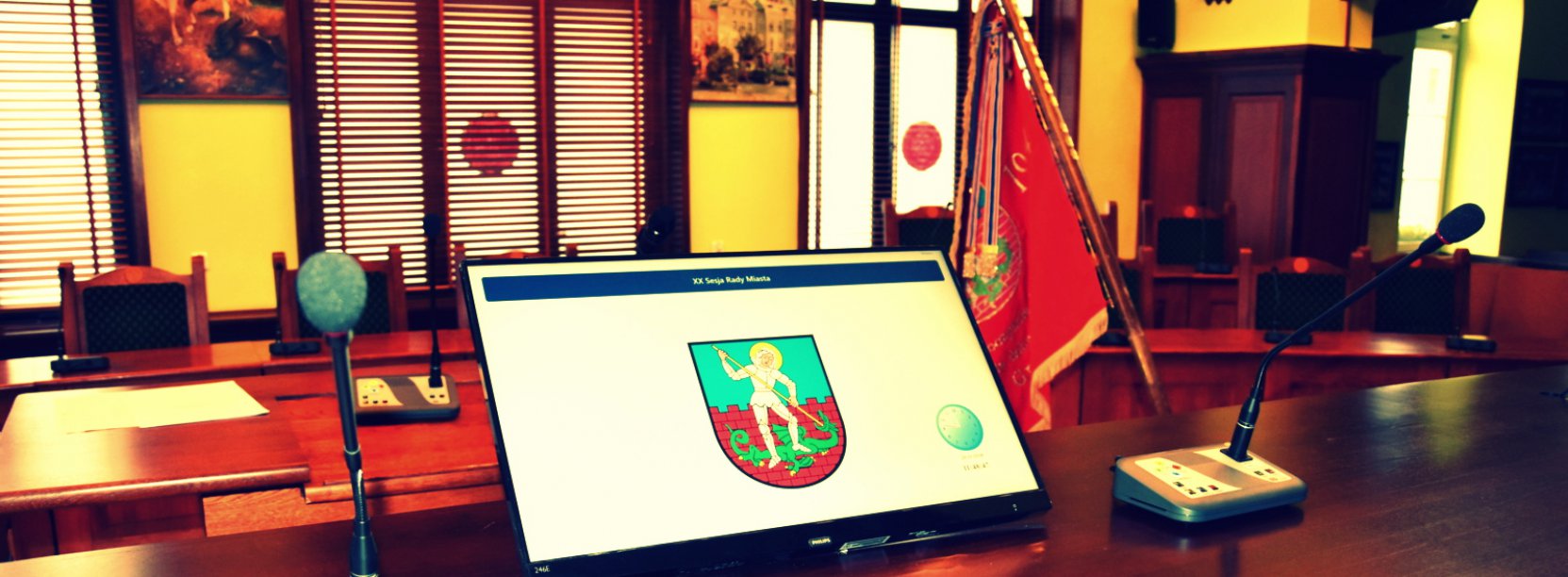 Sala obrad rady miejskiej, na pierwszym planie monitor wyświetlający herb miasta