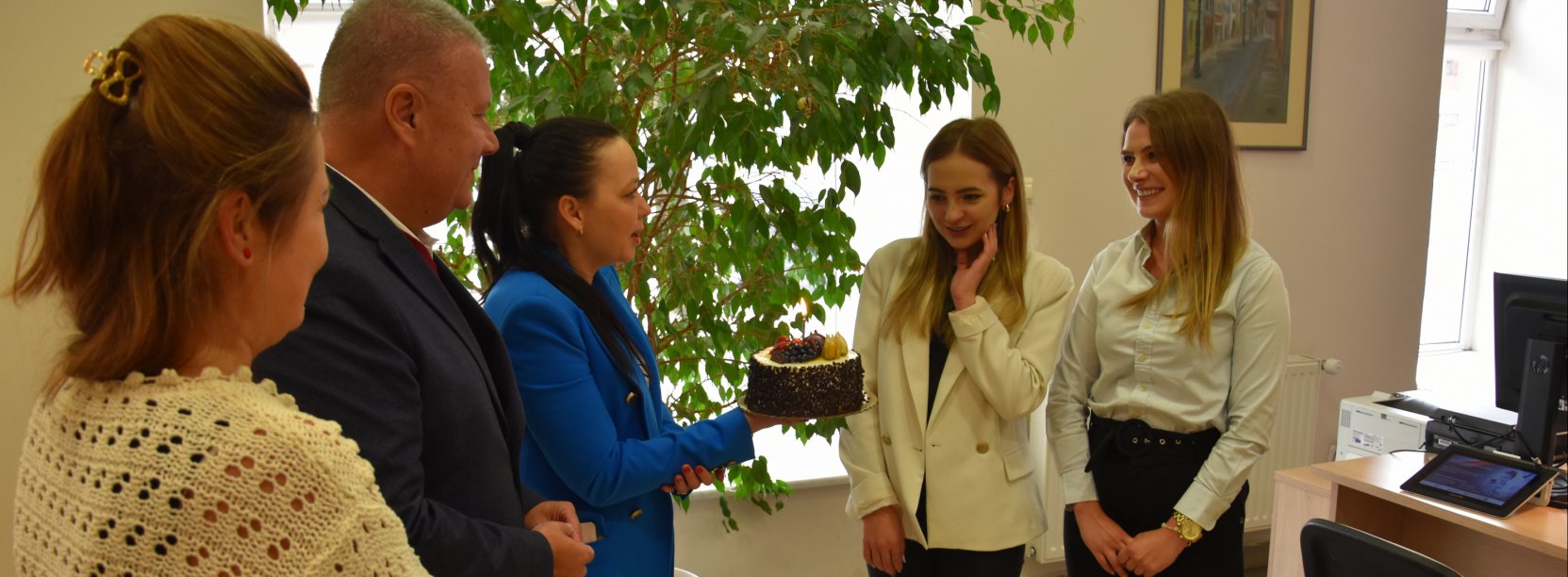 Pięc osób, w tym jeden mężczyna, pani w niebieskiej marynarce trzyma tort