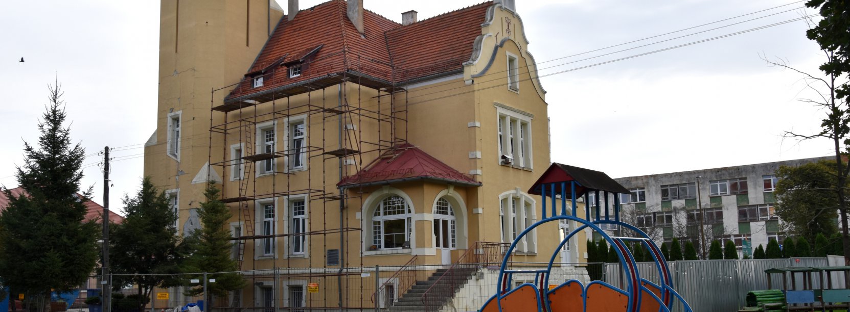 Kamienica z żółtą elewacją i czerwonym dachem, na ścianie kamienicy ustawione rusztowanie