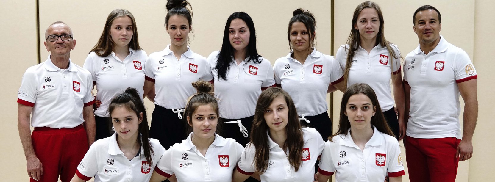 Grupowe zdjecie zawodników i trenerów w białych koszulkach z symbolem godła Polski
