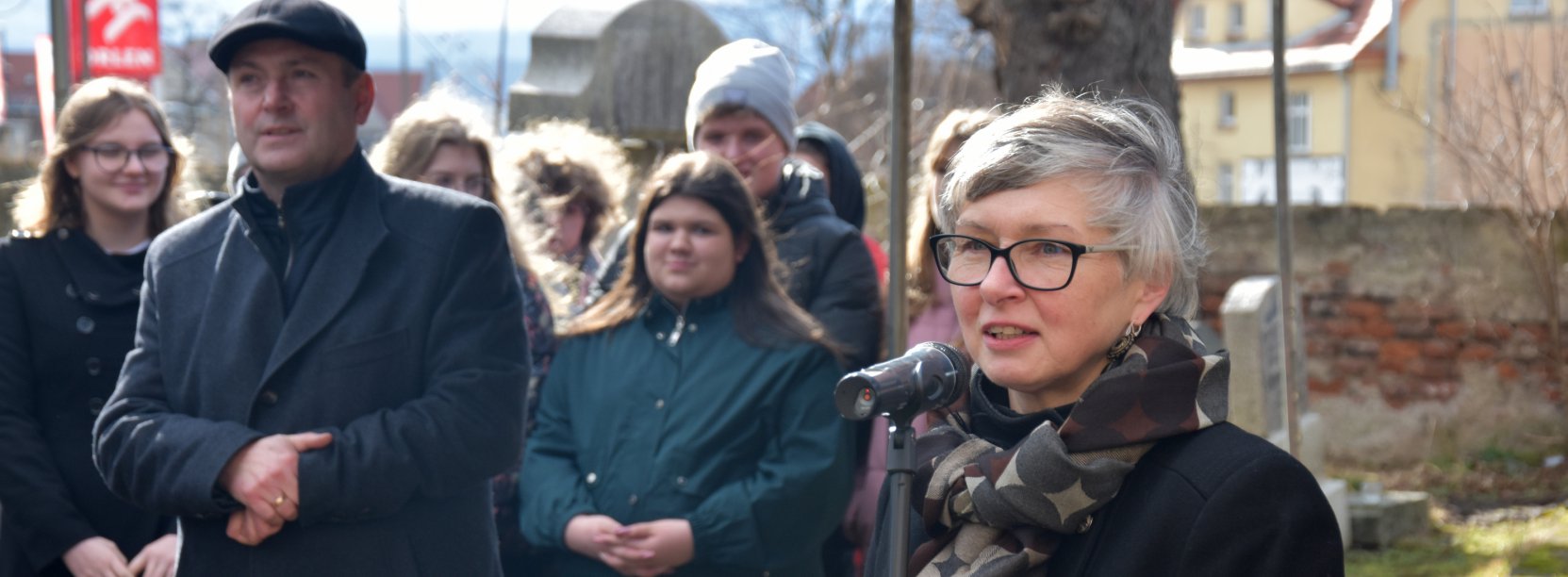 Kobiet mówiąca do mikrofonu, za nią grupka ludzi