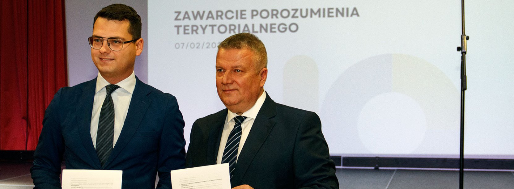 Dwóch mężczyzn w garnituracj trzymających przed sobą dokumenty