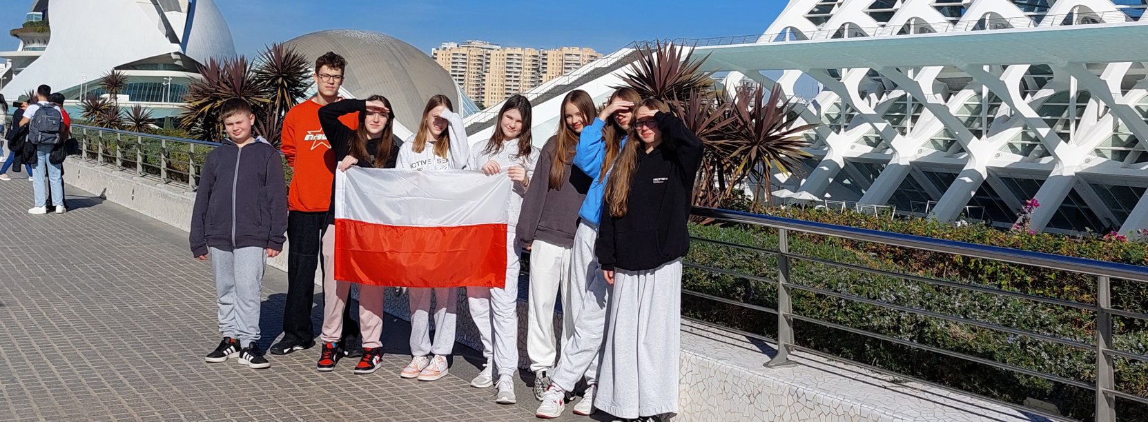 Osmioro uczniów na wspólnym zdjęciu, z przodu flaga Polski, bniebieskie niebo